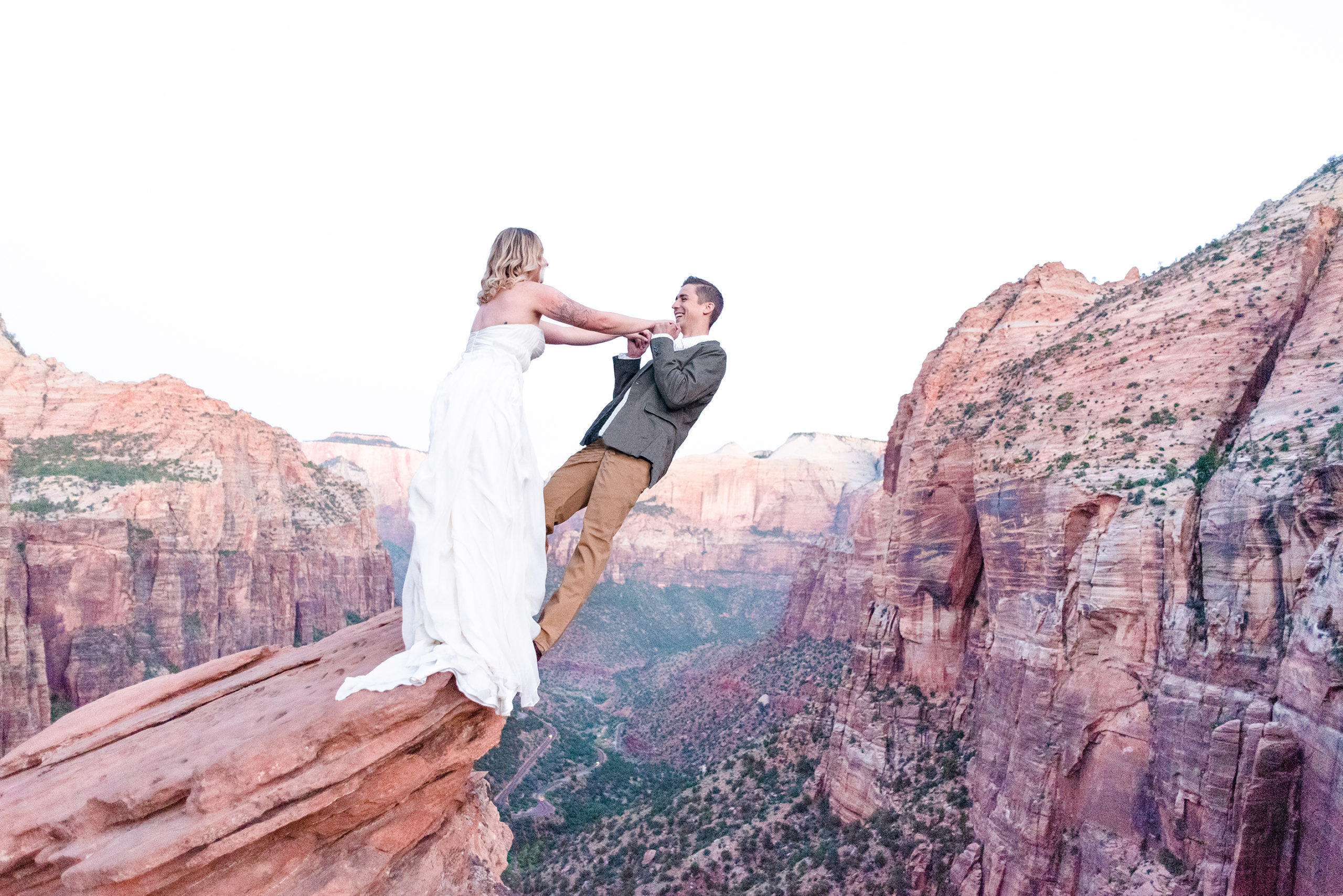 bride dangles groom off of cliff at zion national park in brilliant bridal dress